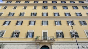 A multi-story building with a yellow facade, multiple windows with shutters, and a central entrance with a decorative arch. - COLOSSEO Apt Mecenate 77 - Home and More (Rome)