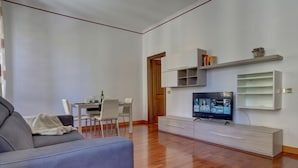 A modern living room with a grey sofa, a dining table with chairs, a TV on a stand, and built-in shelving. - COLOSSEO Apt Mecenate 77 - Home and More (Rome)
