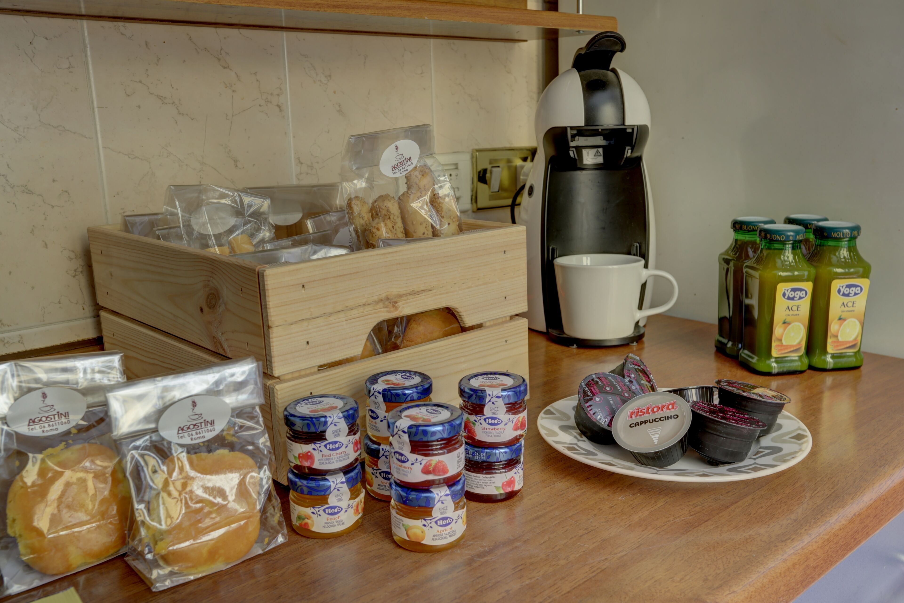 Una encimera de cocina con varios alimentos, entre ellos pan envasado, frascos de mermelada y una cafetera.