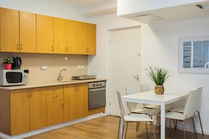 Een compacte keuken met houten kastjes, een magnetron, een koffiezetapparaat en een eethoek met een tafel en stoelen.