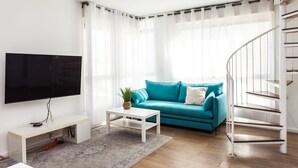Una sala de estar moderna con un televisor de pantalla plana, un sofá verde azulado, una mesa de centro blanca y una escalera.