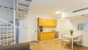 Una cocina moderna con armarios de madera, un comedor con mesa y sillas blancas, y una escalera con barandilla blanca.