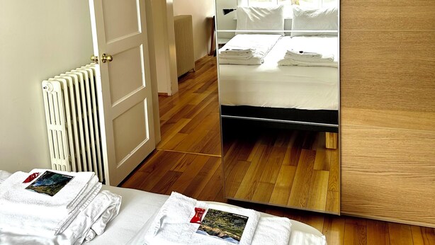 Ein modernes Hotelzimmer mit einem großen Spiegel, einem Bett mit weißer Bettwäsche, einem Heizkörper und einem Holzboden.