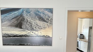 Ein modernes Wohnzimmer mit grauem Sofa, einem großen abstrakten Gemälde an der Wand und Blick in den Küchenbereich.