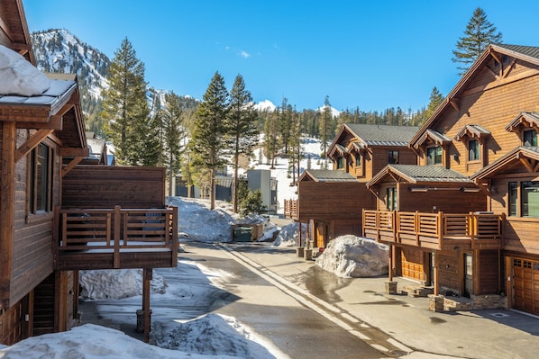 Un chalet en bois doté d’un balcon, une rue enneigée et une chaîne de montagnes en arrière-plan.