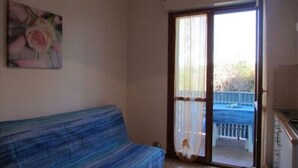 A room with a blue sofa, a painting of a rose, and a sliding glass door leading to an outdoor area. - Studio in a Poolside Residence (San Michele al Tagliamento)