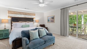 Une chambre à coucher avec un lit, un canapé bleu, un ventilateur de plafond, une table de chevet, une lampe, un tableau et une vue sur l’extérieur.