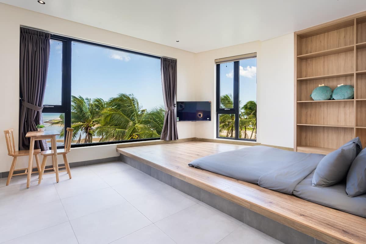 A modern bedroom with a large bed, a TV, and a view of palm trees.