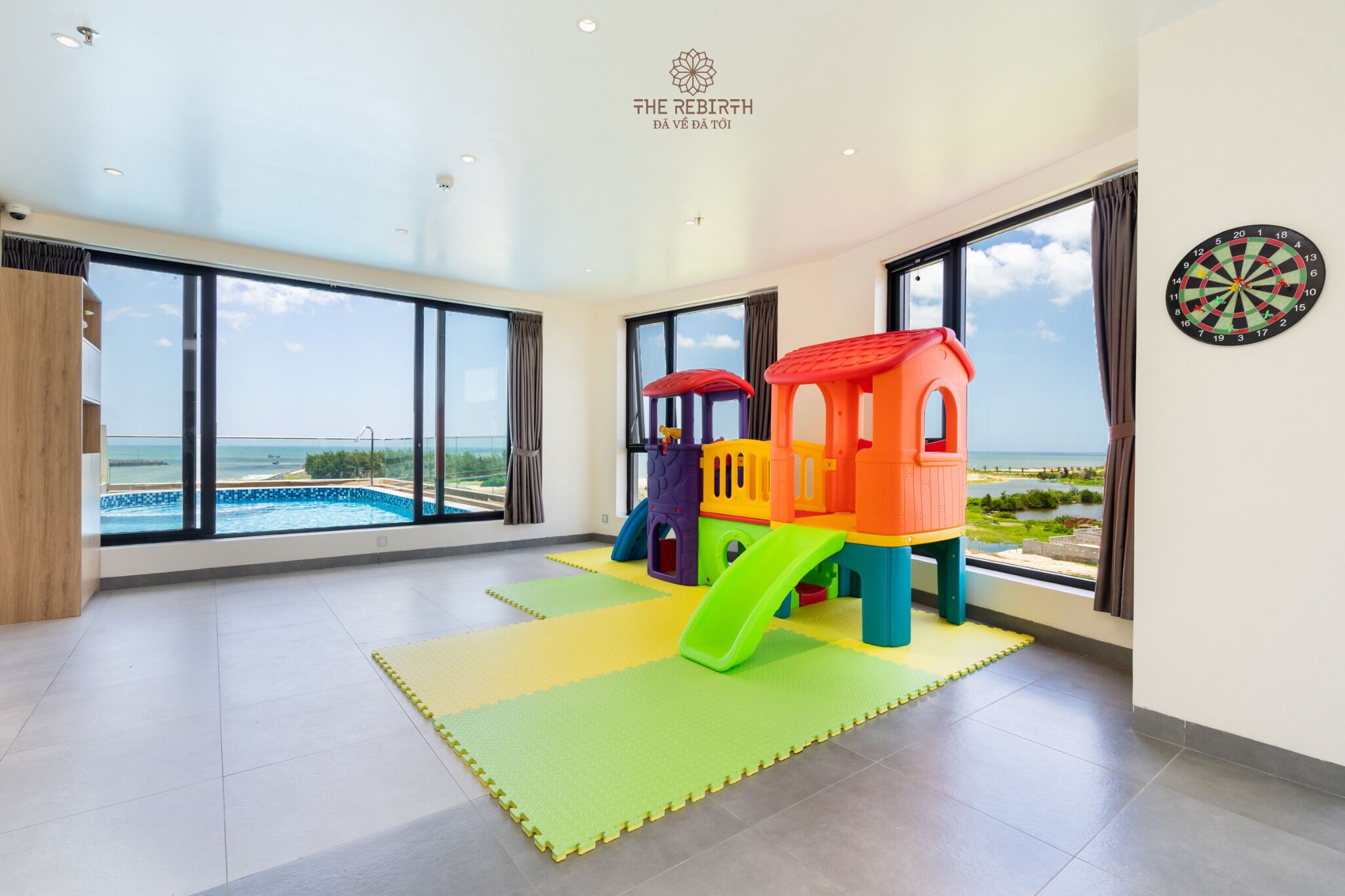 A spacious room with large windows, a colorful play structure, and a dartboard.