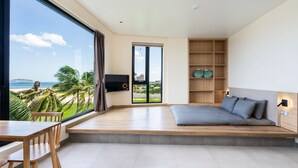 A modern bedroom with a large window, a bed, a desk, and a TV. - The Rebirth Apartment Binh Chau Ho Tram (Ho Chi Minh City)