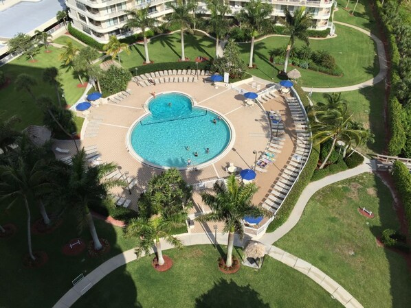 An aerial view of a resort with a central swimming pool surrounded by lounge areas and palm trees.