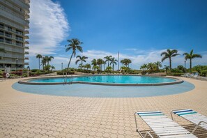 A swimming pool with lounge chairs, palm trees, and a hotel building in the background.
