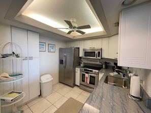 A modern kitchen with white cabinets, stainless steel appliances, a ceiling fan, and a marble countertop. - Beachfront 2BR/2BA condo with pool, Wi-Fi, and beach access. (Marco Island)
