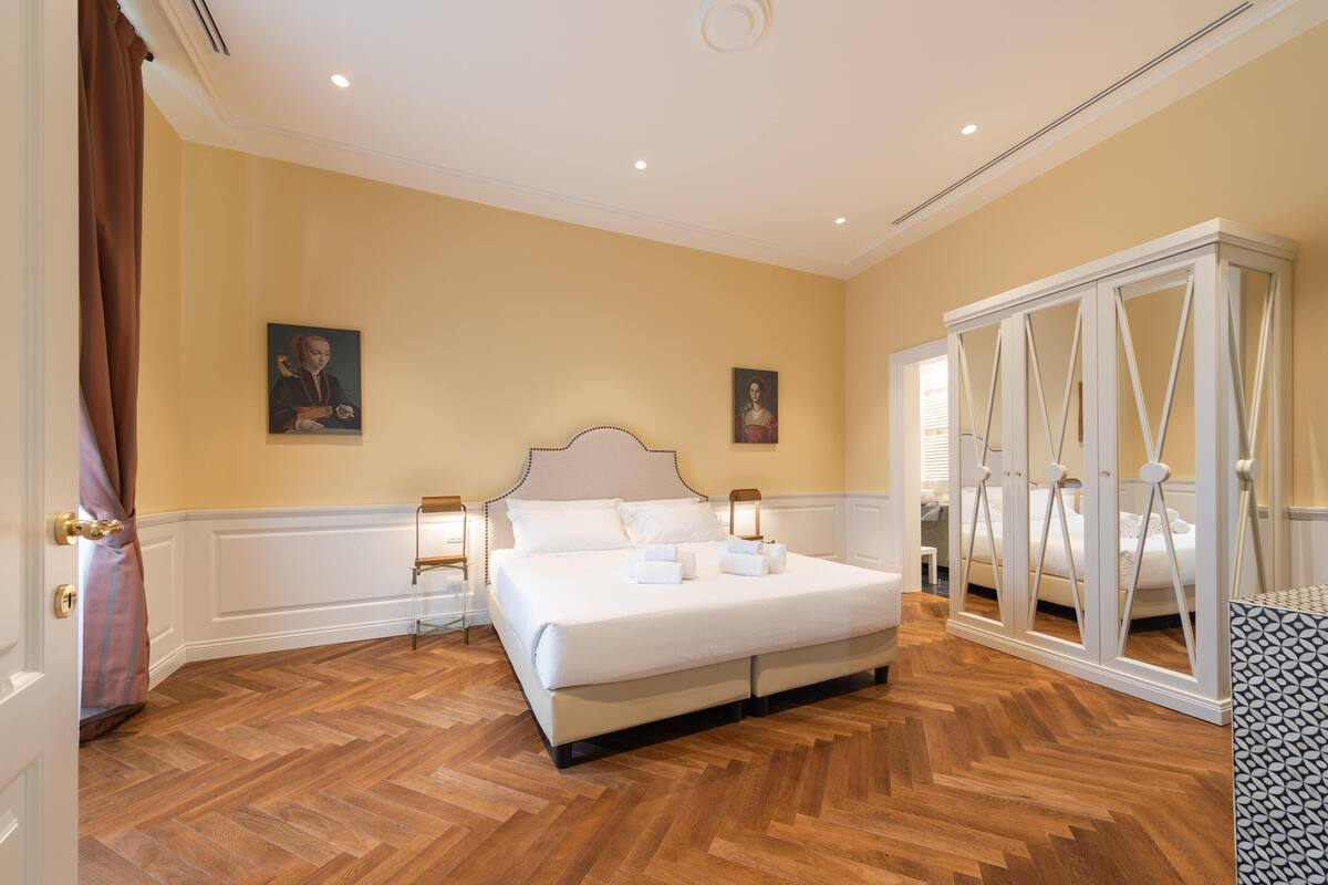 Un ampli dormitori amb un llit gran, sòcols de parquet de fusta i un armari blanc clàssic.