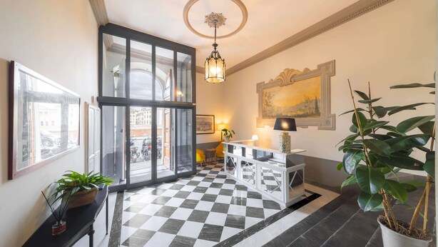 A hotel lobby with a checkered floor, a large window, a reception desk, and a potted plant. - Algilà Luxury Torrigiani Apartments (Florence)