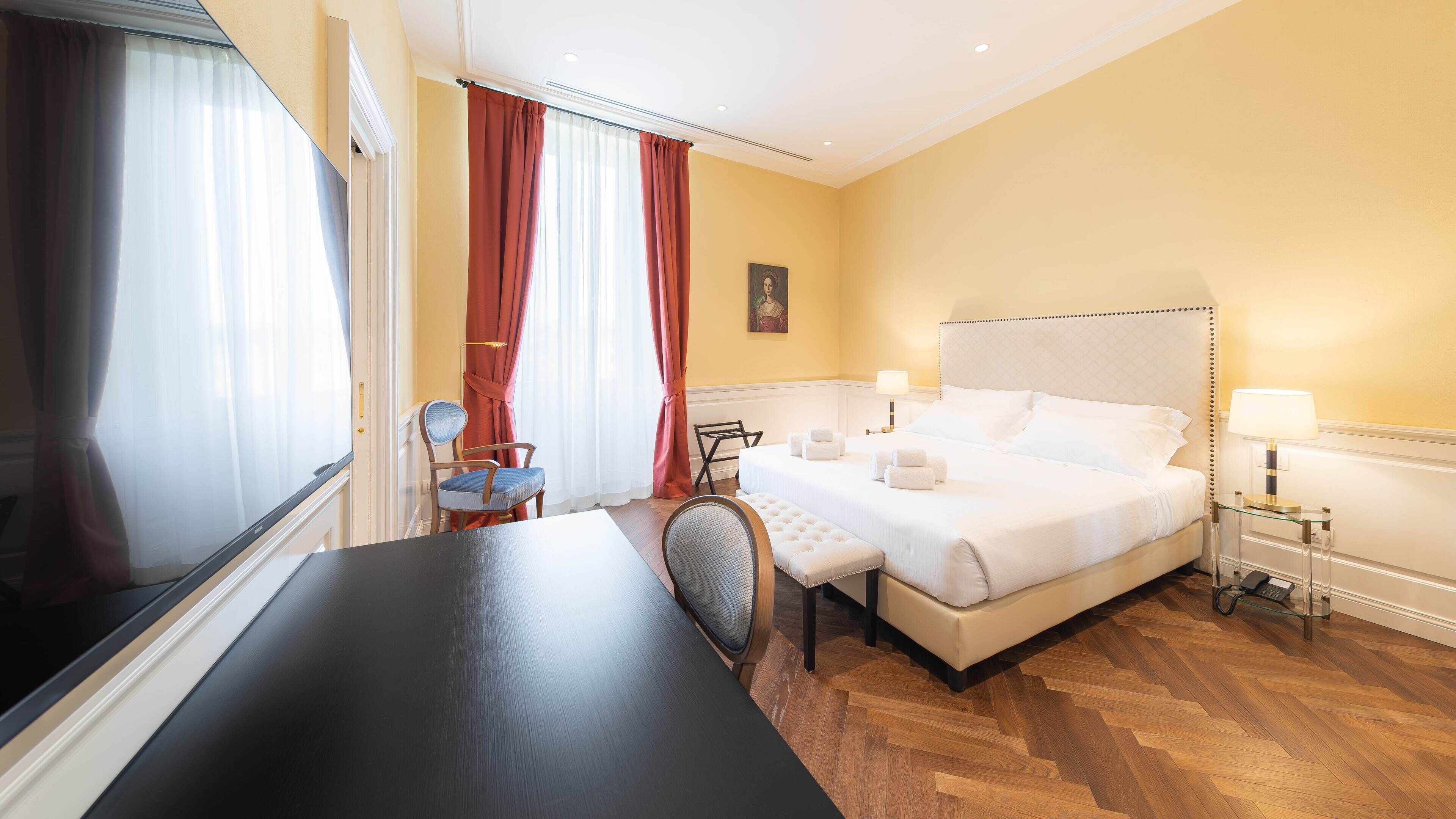 A hotel room with a bed, bedside tables, a chair, a desk, and a window with curtains.