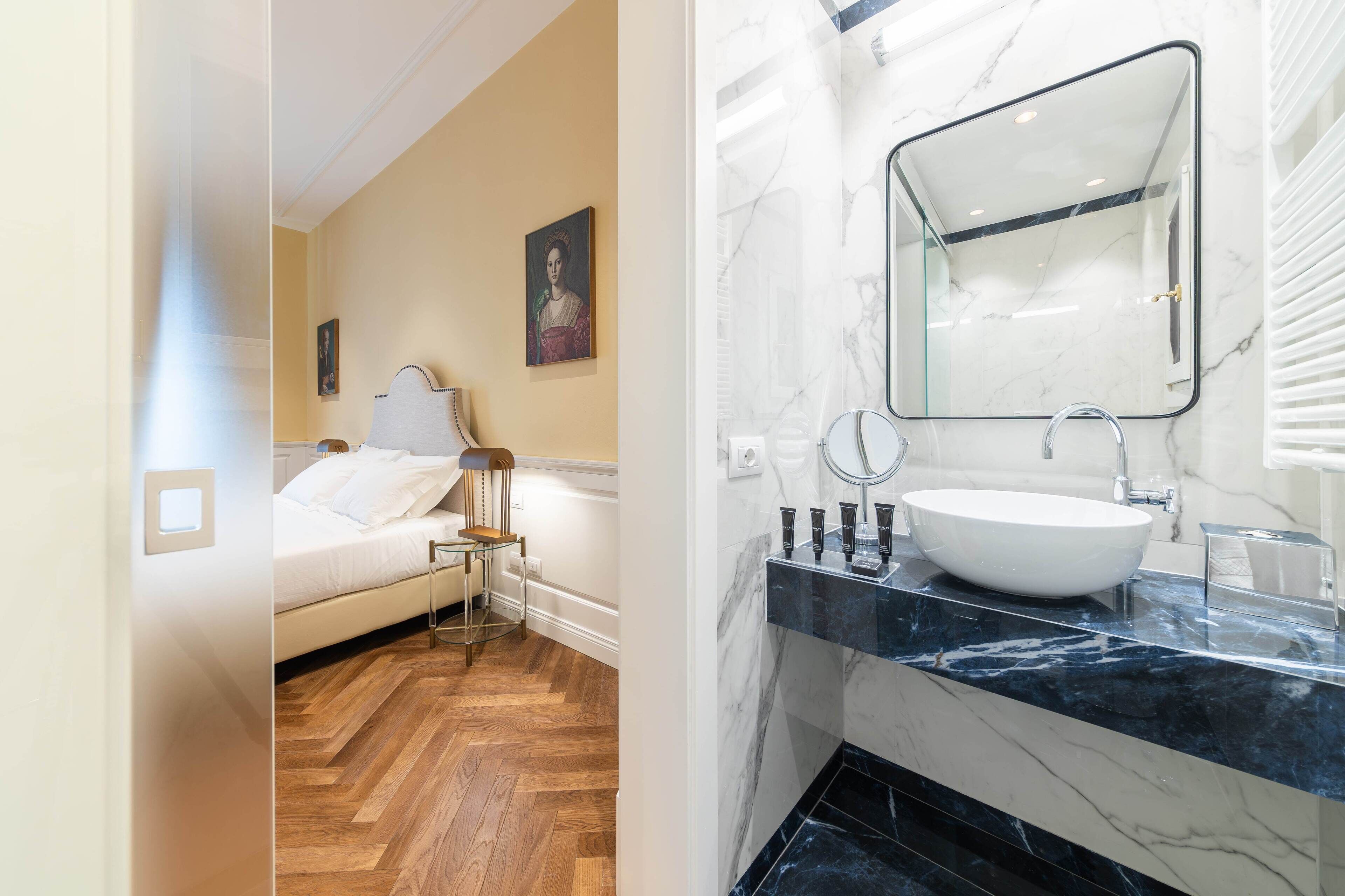 A modern bedroom with a wooden floor and a bed, and a bathroom with a marble sink and large mirror.