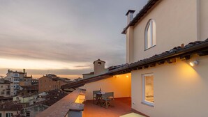 A rooftop terrace with a table and chairs, a small window, and a view of the cityscape. - Algilà Luxury Torrigiani Apartments (Florence)