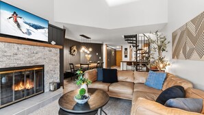 Un salon moderne doté d’une cheminée, d’un canapé en cuir, d’un coin repas et d’un escalier menant à un niveau supérieur.