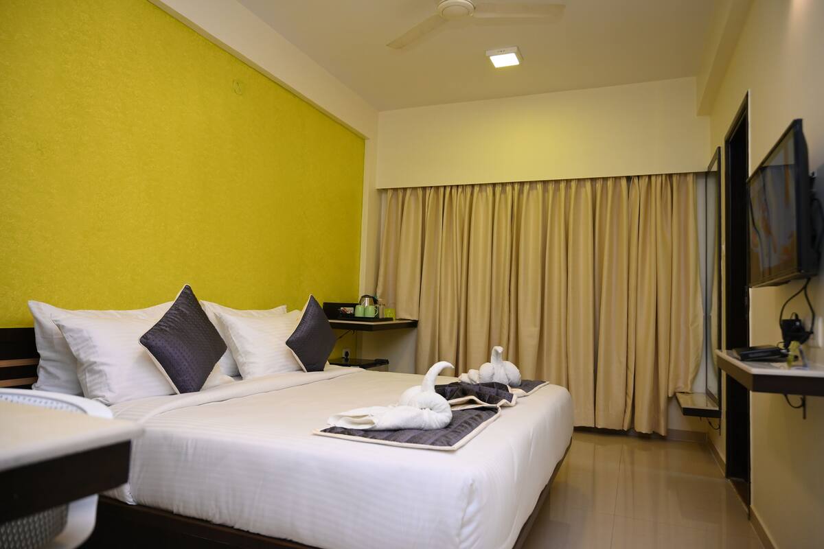 A hotel room with a bed, a bedside table, a TV, and a window with curtains.
