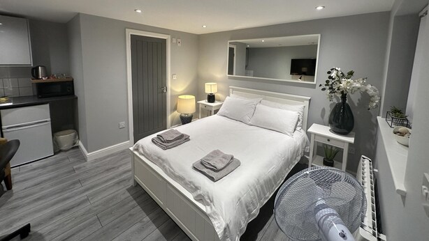 A modern bedroom with a bed, bedside table, lamp, and a large mirror. - Beautiful 1-bed Modern Luxury Apartment in Luton (Luton)