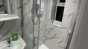 A modern bathroom with a glass-enclosed shower, marble walls, a white sink, and a small window. - Beautiful 1-bed Modern Luxury Apartment in Luton (Luton)