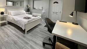 A bedroom with a bed, bedside tables, a desk, a chair, a mirror, and a door. - Beautiful 1-bed Modern Luxury Apartment in Luton (Luton)