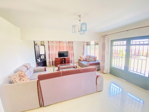 A spacious living room with a large sofa, a television, and a dining table.