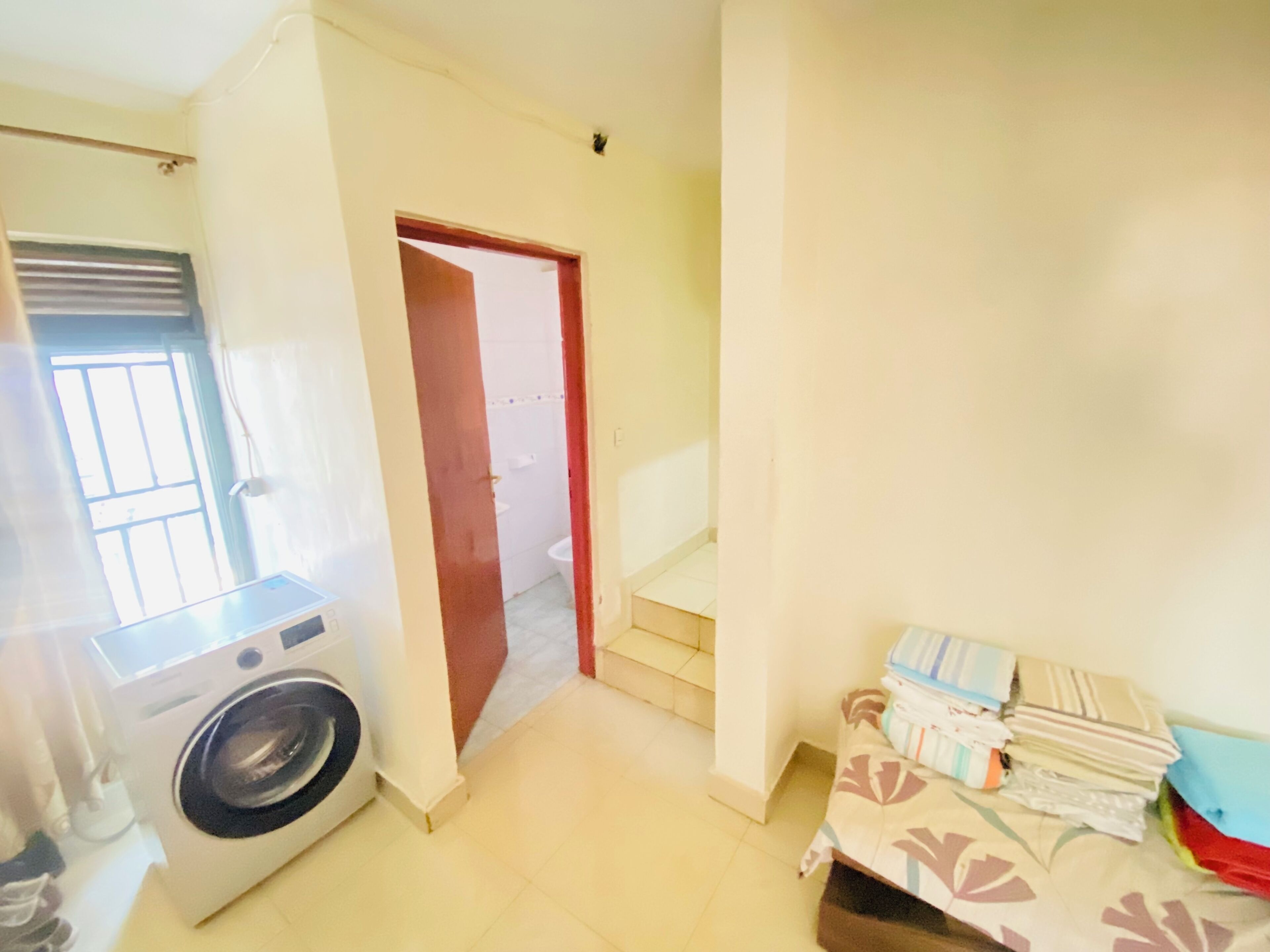 A laundry room with a washing machine, a door leading to a bathroom, and a bed with neatly folded blankets.