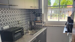 A modern kitchen with dark cabinets, a granite countertop, a built-in oven, a sink, and a window with a view of trees. - Haus Seelöwe für 3 Personen, Strandnah, Terrasse, Grill, Fahrräder, Wlan, top (Dornum)