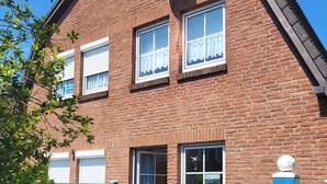 A two-story brick house with a blue gate, large windows, and a visible front door. - Haus Seelöwe für 3 Personen, Strandnah, Terrasse, Grill, Fahrräder, Wlan, top (Dornum)