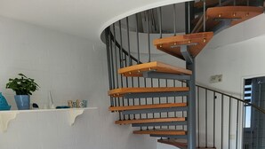 A modern interior with a wooden dining table, white chairs, a TV, a spiral staircase, and a patterned rug. - Haus Seelöwe für 3 Personen, Strandnah, Terrasse, Grill, Fahrräder, Wlan, top (Dornum)