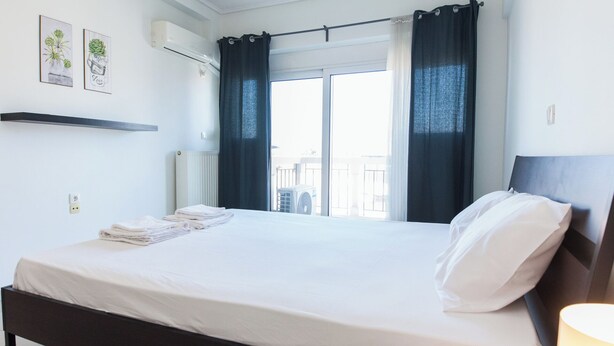 A neatly made bed with white linens, a dark headboard, and a window with dark curtains. - Modern Equipped apt w Balcony GC 3120-02 (Athens)