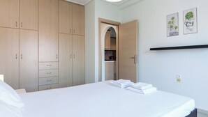 A bedroom with a bed, a wardrobe, a shelf with plants, and a doorway leading to a bathroom. - Modern Equipped apt w Balcony GC 3120-02 (Athens)