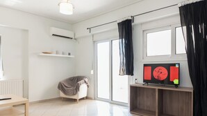 A modern living room with a flat-screen TV, a sofa, a coffee table, and a window with black curtains. - Comfy New Apt w Balcony GC 3360-01 (Athens)