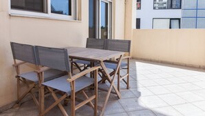 A wooden table and chairs set on a tiled patio with a building in the background. - Comfy New Apt w Balcony GC 3360-01 (Athens)