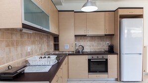 A modern kitchen with light wood cabinets, a stainless steel sink, a built-in oven, and a white refrigerator. - Comfy New Apt w Balcony GC 3360-01 (Athens)