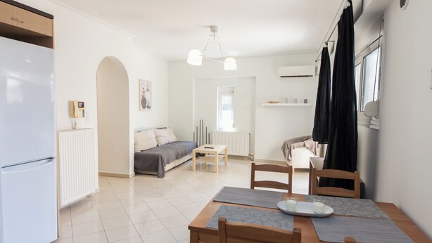 A modern kitchen with a refrigerator, a dining table with chairs, a sofa, and a window with curtains. - Comfy New Apt w Balcony GC 3360-01 (Athens)