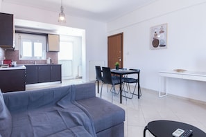 A modern living room with a grey sofa, a dining area with a table and chairs, a kitchen in the background, and a door leading to another room. - Gorgeous Apt w Magical View GC 3332-02 (Athens)