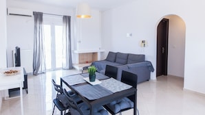 A modern living room with a sofa, a dining table with chairs, a fireplace, and a large window with curtains. - Gorgeous Apt w Magical View GC 3332-02 (Athens)