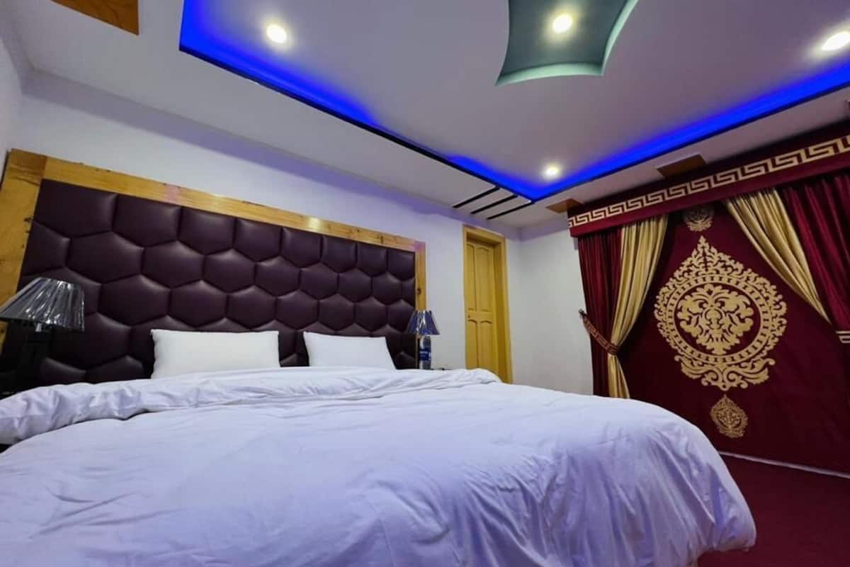 Ein modernes Hotelzimmer mit einem großen Bett, einem Kopfteil mit geometrischem Muster und einer Decke mit Einbuchtungslichtern.