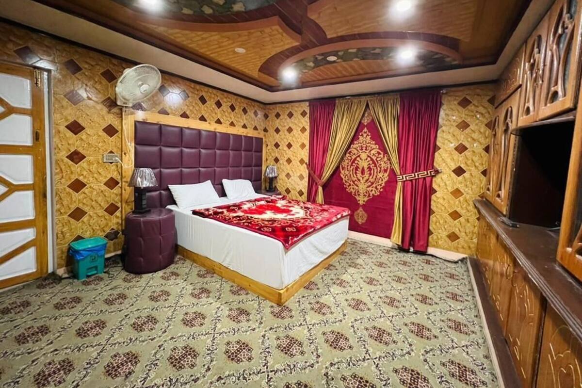 Ein Schlafzimmer mit Bett, Ventilator, Nachttisch, Fernseher und Wand- und Deckenverkleidung mit Muster.