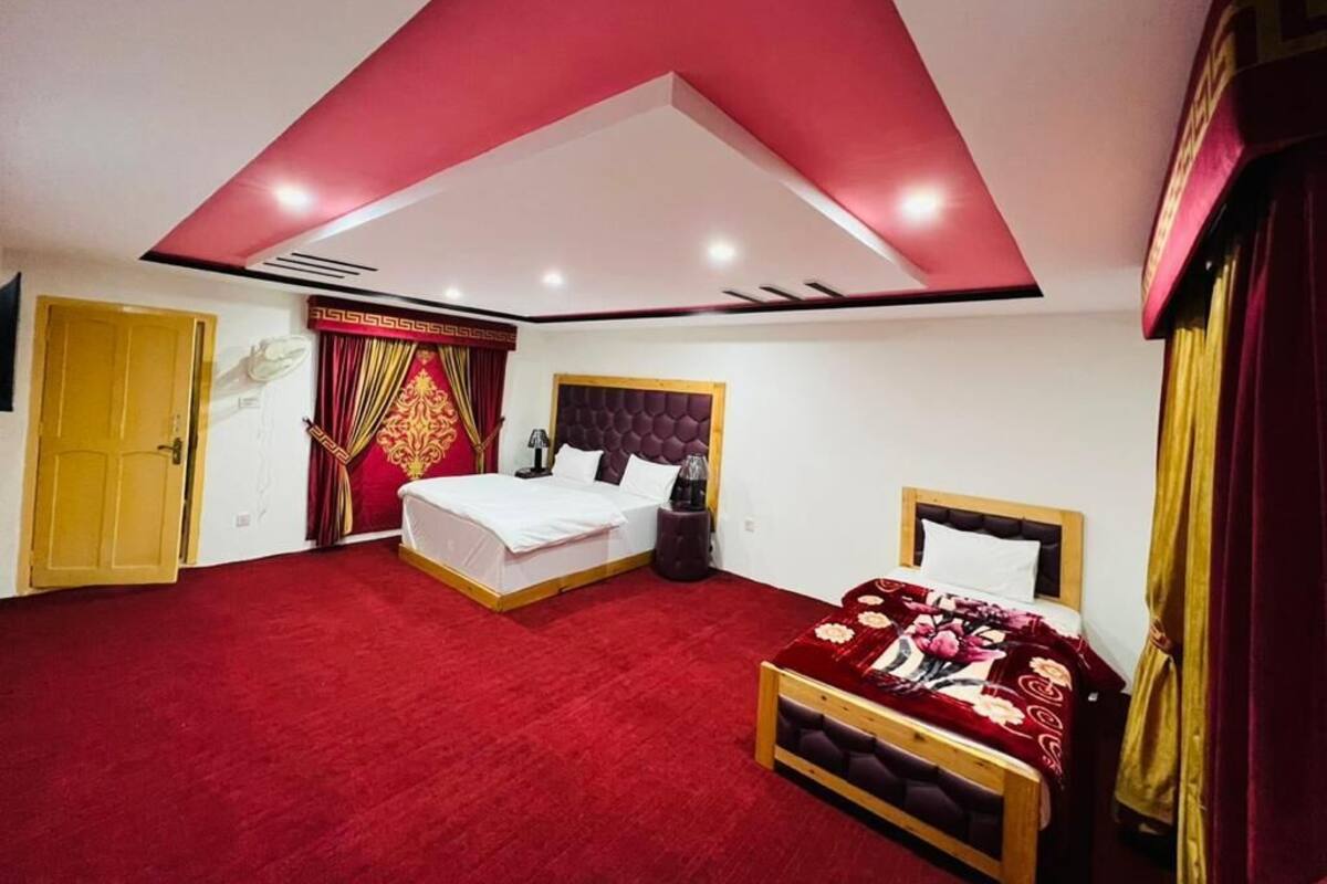 Ein Schlafzimmer mit rotem Teppich, zwei Betten, einem hölzernen Kopfteil und einer roten Decke.