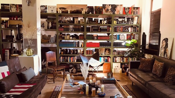 A cozy living room with a large bookshelf filled with books and decorative items, a comfortable sofa, and a coffee table with candles and books. - Unique yoga loft! Quiet room for courses, seminars, workshops! (Sinsheim)