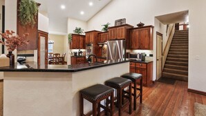 Una cocina con armarios de madera, un refrigerador de acero inoxidable y una zona de bar con taburetes.