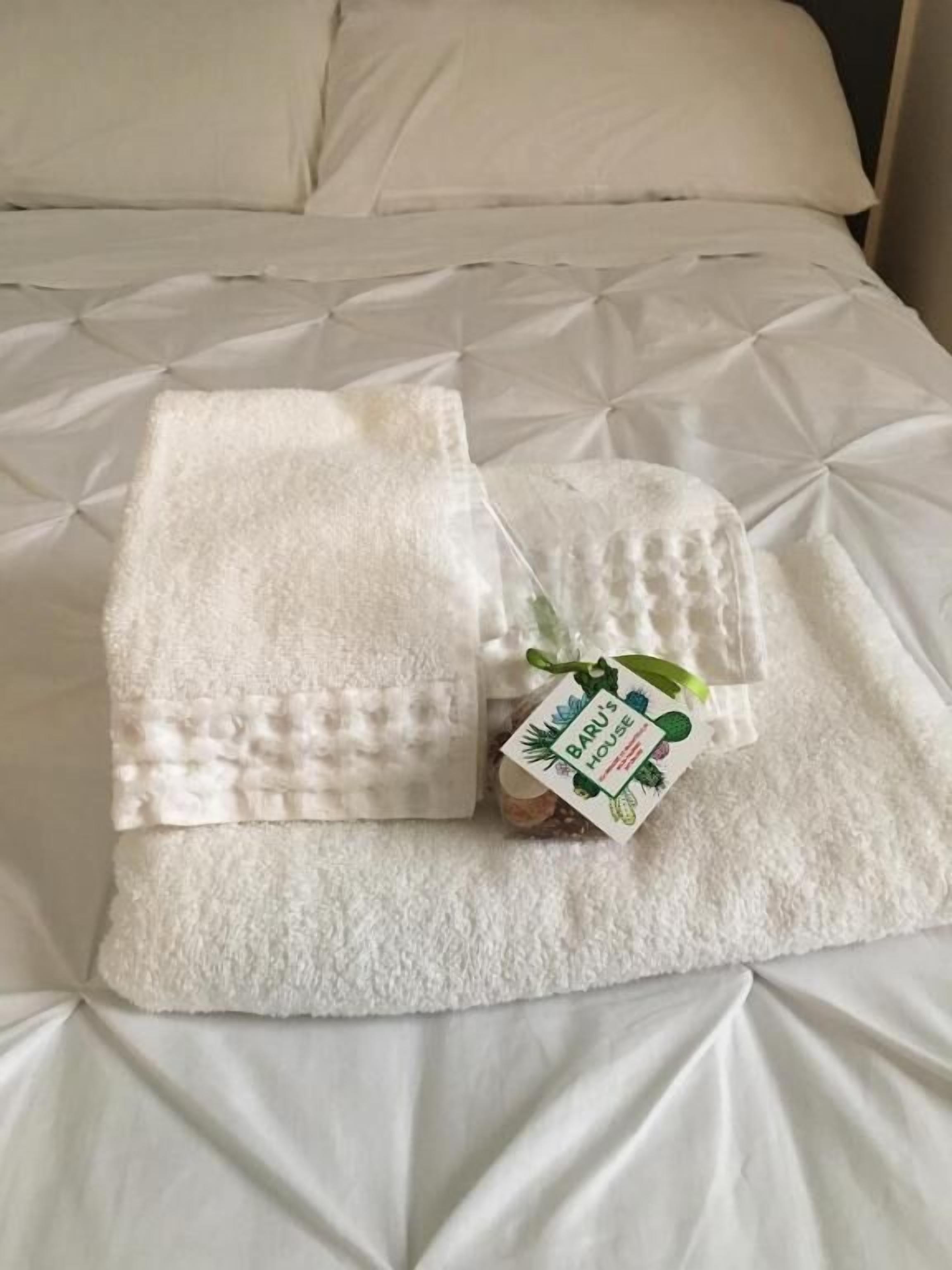 A neatly folded white towel with a tag on a bed with a quilted pattern.