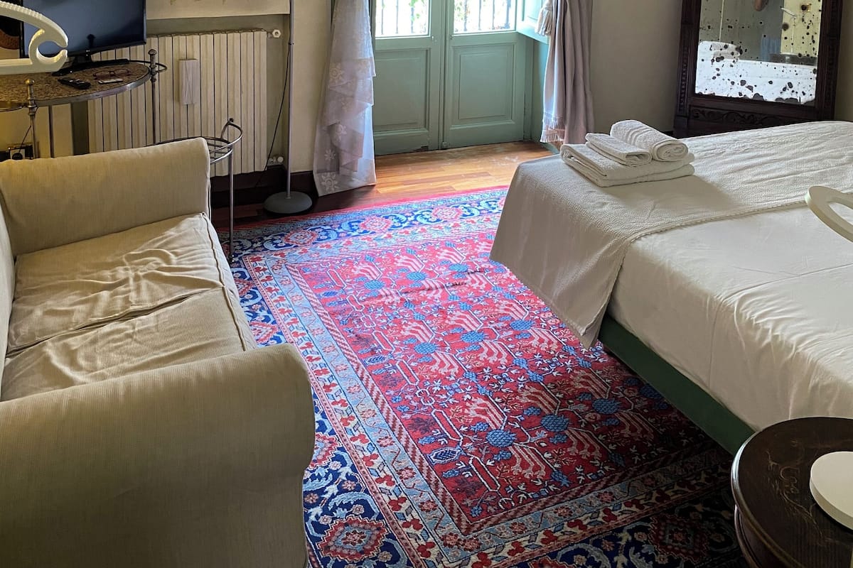 Hotellihuone, jossa on sänky, sohva, televisio, peili ja kuviollinen matto.