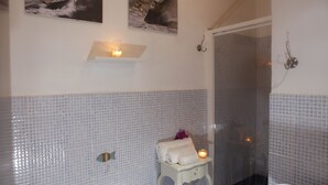 A bathroom with tiled walls, a small table with a towel, a candle, and a shower area. - Chic Villa Antonina Studio No2163 (Golfo Aranci)