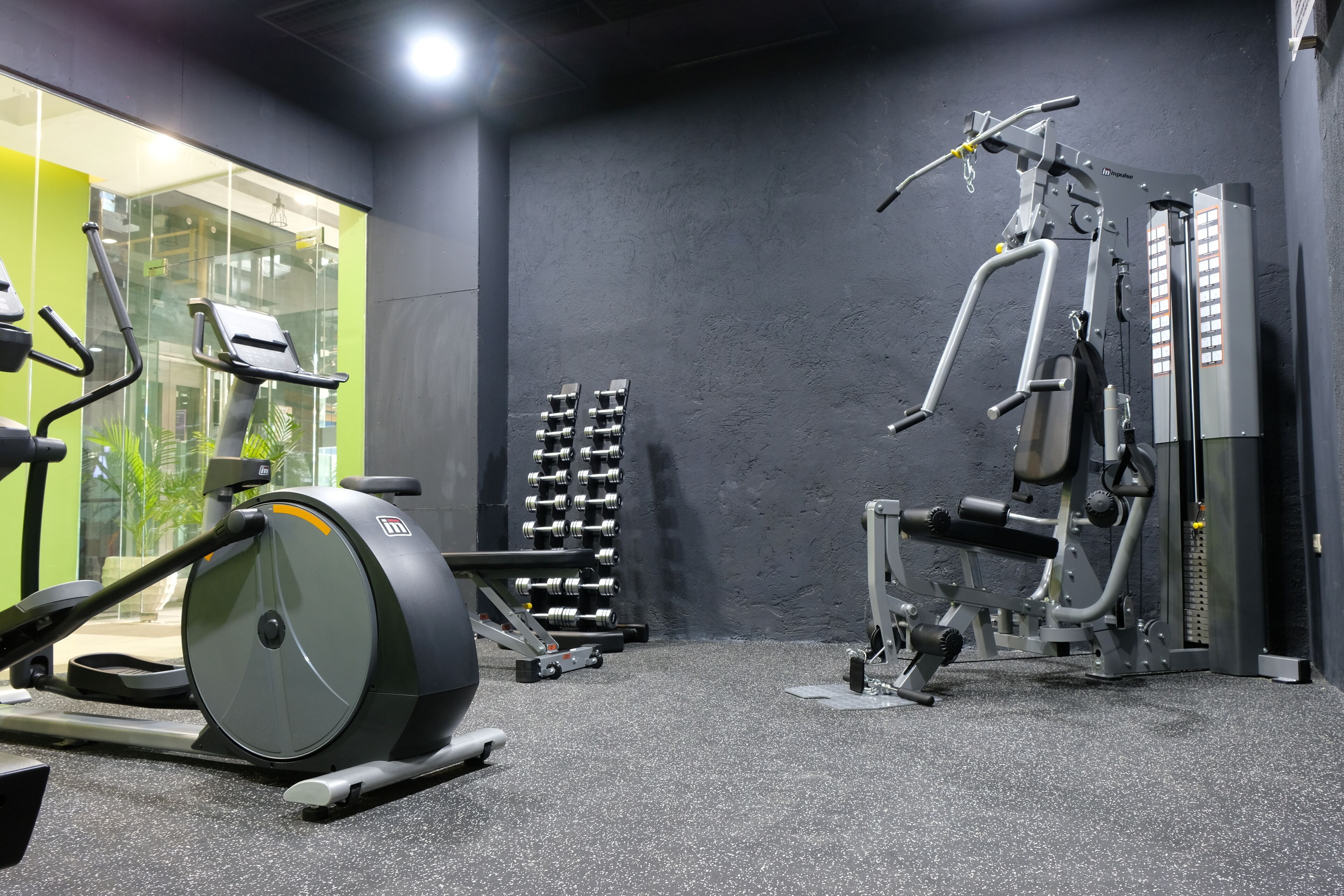 A gym with exercise equipment, including an elliptical trainer, dumbbells, and a weight machine.