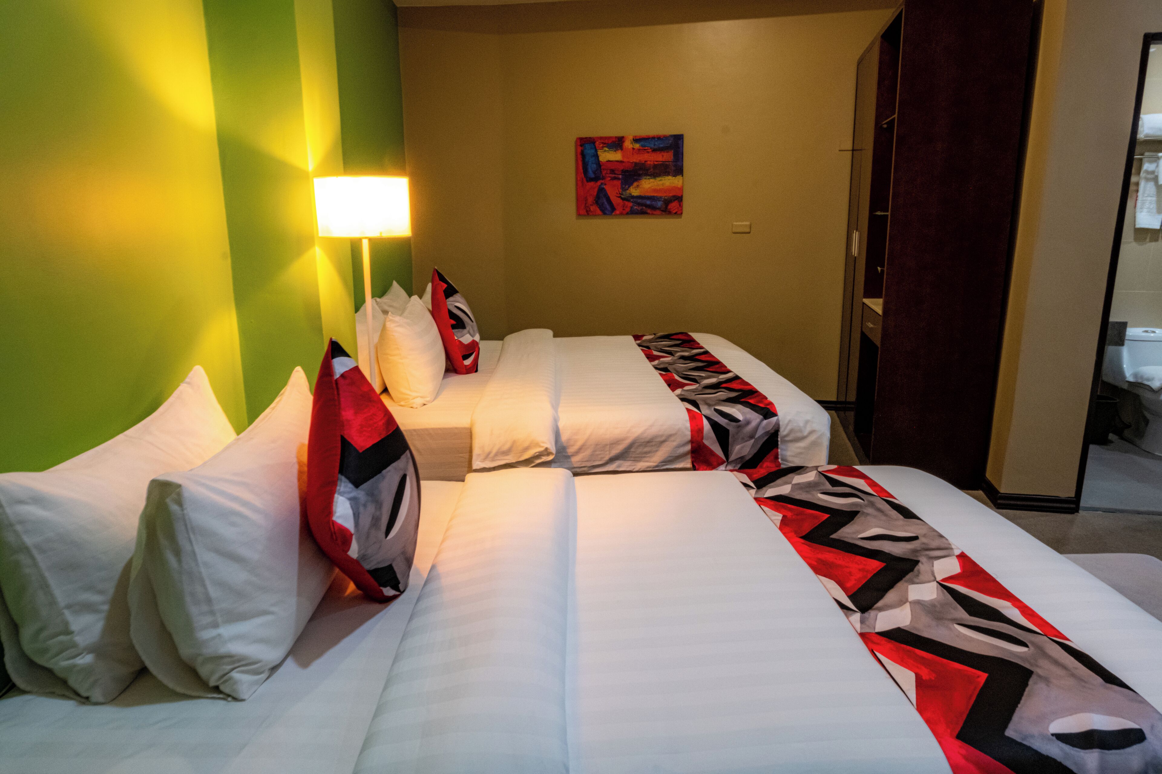 A hotel room with two beds, a green wall, a painting, and a mirror.